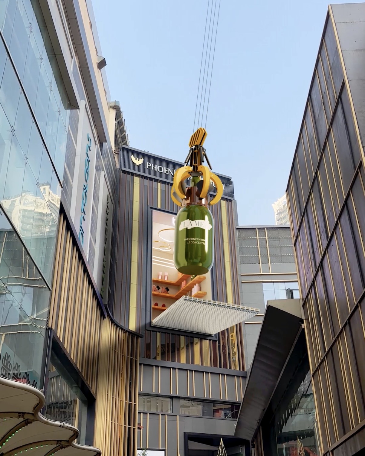Large-format anamorphic visual of a mechanical claw lifting a green bottle above the Phoenix street frontage